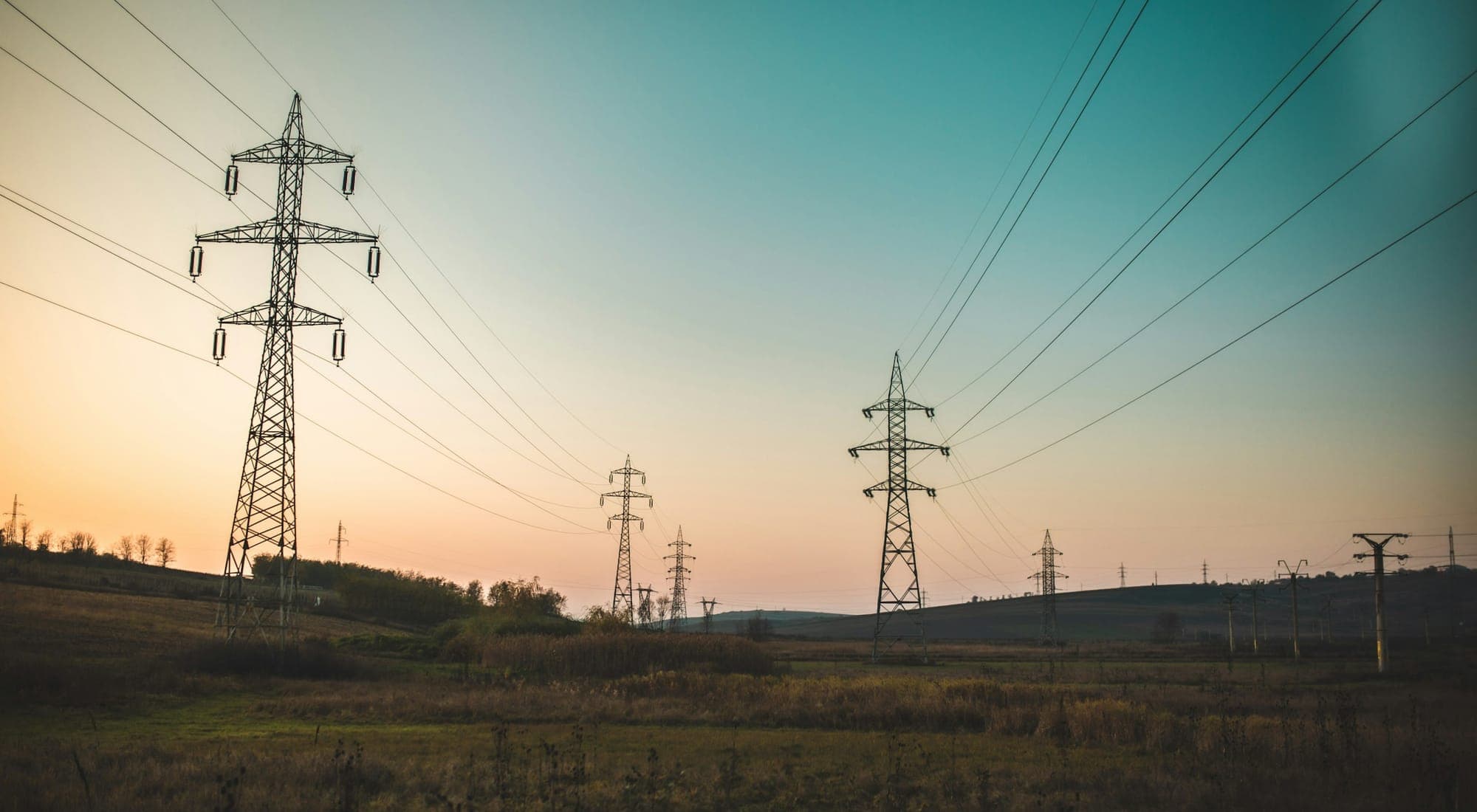 High-voltage transmission pylons carrying lines across open farmland at dusk