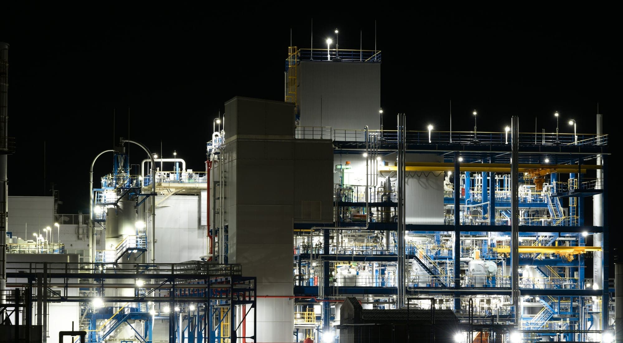 A large process complex lit at night, pipe racks and structures against a black sky