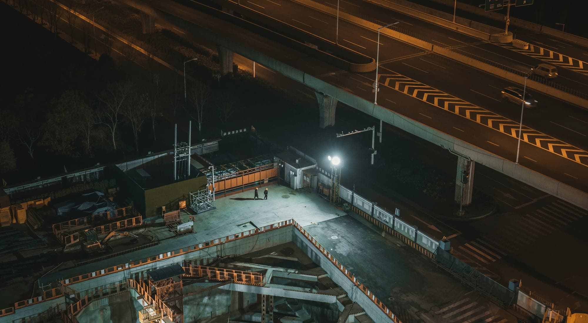 A construction site seen from above at night, excavation and slabs under floodlight
