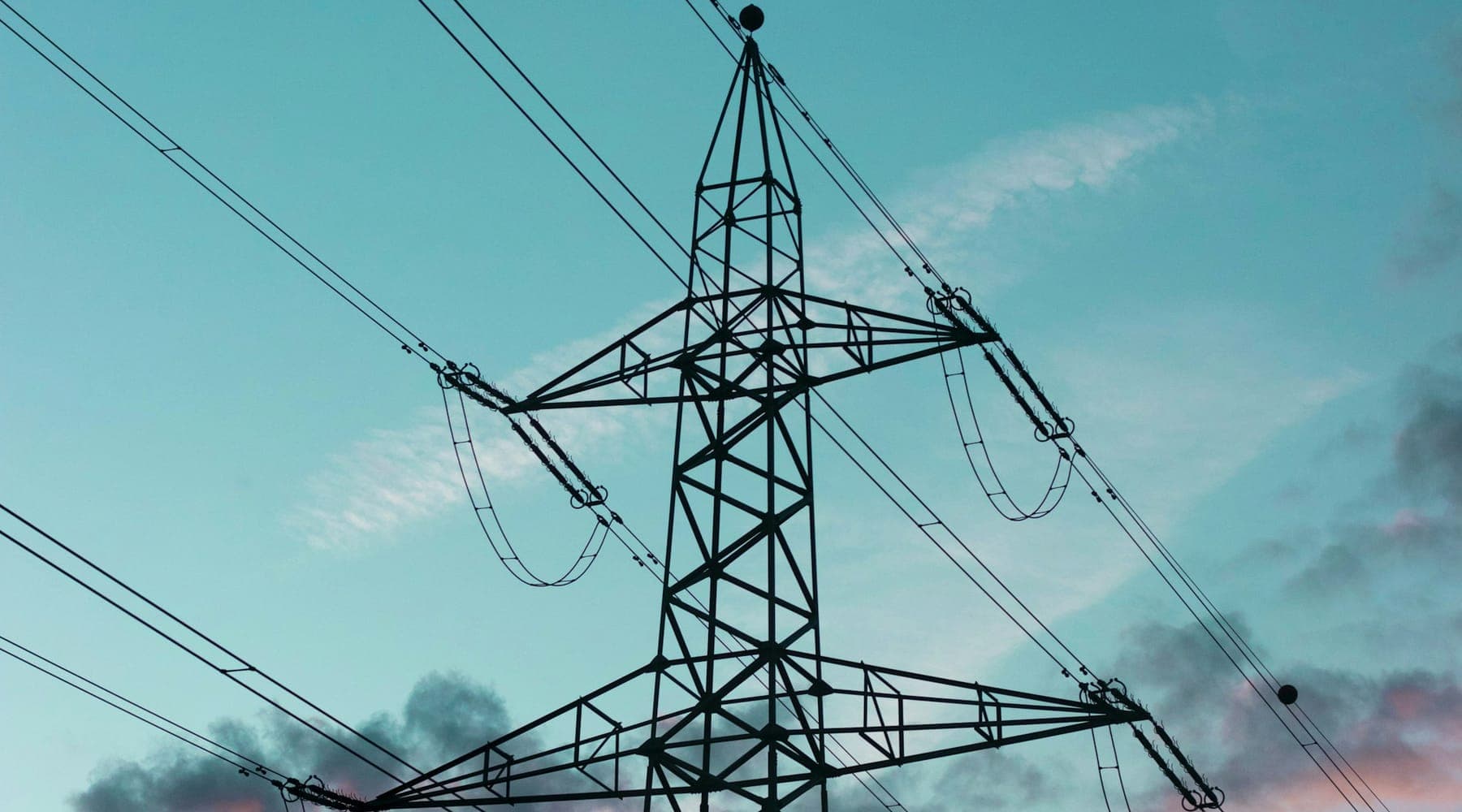A high-voltage transmission pylon and its conductors against a dusk sky